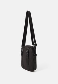 Černá crossbody taška z nylonu s hladkým povrchem, nastavitelným popruhem a dvěma předními kapsami se zacvakávacími uzávěry.