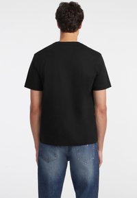 Melna kokvilnas T-krekls ar īsām piedurknēm un apaļu kakla izgriezumu, kam ir brīvs piegriezums un gluda tekstūra. Valkāts kopā ar gaiši ziliem džinsiem.