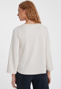 Lichtbeige, langof mouwtop met een ronde halslijn en een slim fit. Gladde textuur, zachte stof en een schone zoom. Draagt men met donkere corduroy broek.