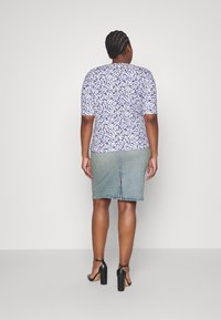 Blommig kortärmad topp i lila och vitt, ihop med en ljusblå denimpennkjol. Modellen bär svarta högklackade sandaler.