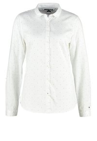 Camisa blanca de botones con mangas largas, patrón de pequeños puntos dorados y cuello clásico. Presenta un dobladillo recto y cierre de botones.
