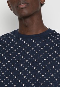 Sudadera azul marino con un pequeño patrón repetitivo de estrellas en crema clara, con una textura de algodón suave y un cuello redondo clásico.