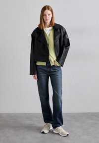 Svart skinnjakke med kort lengde, grønn ribbestrikket cardigan, hvit skjorte, blå jeans og beige sneakers. Uformell lagdelt antrekk med varierte teksturer.