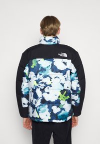 Chaqueta acolchada con un patrón floral en azul, blanco y verde; área de hombros y cuello en negro; presenta un logo en la parte superior de la espalda.