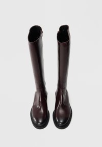 Bottes en cuir bourgogne montant jusqu'au genou, avec une texture lisse, un bout arrondi et une semelle en caoutchouc noire. Elles disposent d'une fermeture éclair sur le côté pour un enfilage facile.
