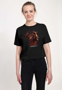 Czarny bawełniany t-shirt z graficznym wzorem rogatej istoty trzymającej laskę, z napisem "Dungeons & Dragons" i czerwonymi akcentami.