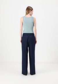 Lyseblå ribbet tanktop med ermeløs design, sammen med høyveide marineblå vide bukser. Glatt tekstur og skreddersydd passform.