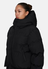 Czarna kurtka puchowa z wysokim kołnierzem, zamkiem błyskawicznym w bocznej kieszeni oraz pikowanym wzorem. Posiada gładką, wodoodporną fakturę.