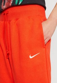 Ljusa orange Nike sweatpants med en ribbad midjeband, dragsko-detalj, sidficka och vit logotypaccent på vänster lår.