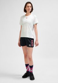 Vit sporttröja med mintgröna detaljer, ihop med svarta shorts med rosa chevronmönster och mönstrade rosa och marinblå strumpor.