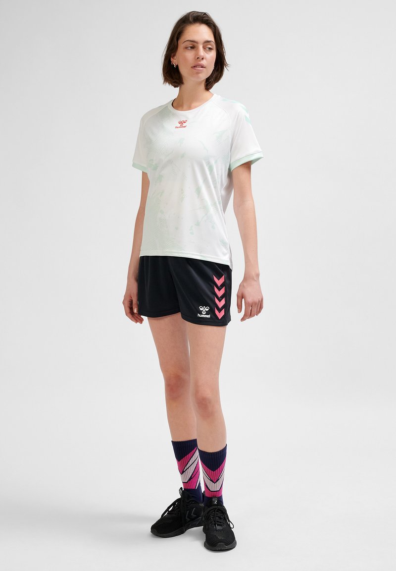 Vit sporttröja med mintgröna detaljer, ihop med svarta shorts med rosa chevronmönster och mönstrade rosa och marinblå strumpor.