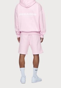 Felpa oversize rosa chiaro e pantaloni corti coordinati, in misto cotone, con logo bianco "PEGADOR" sulla schiena, abbinati a sneakers bianche e calze.