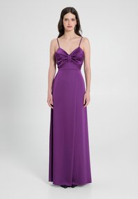 Abito da sera in satin viola con corpetto aderente, dettaglio annodato sul petto e spalline sottili, che si estende in una gonna lunga fino al pavimento.