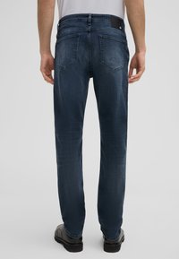 Dunkelblaue Denim-Jeans mit geradem Schnitt, ausgestattet mit Gesäßtaschen, einem schwarzen Lederpatch am Bund und minimaler Verwaschung.