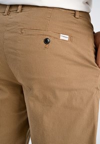 Pantalons à motif tan avec une finition texturée, dotés d'une poche arrière, d'un bouton noir et d'une petite étiquette de marque.
