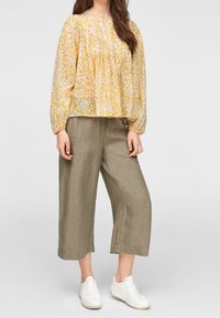 Blusa a maniche lunghe con motivo floreale giallo e texture arricciata, abbinata a pantaloni larghi in lino color khaki e sneaker bianche.