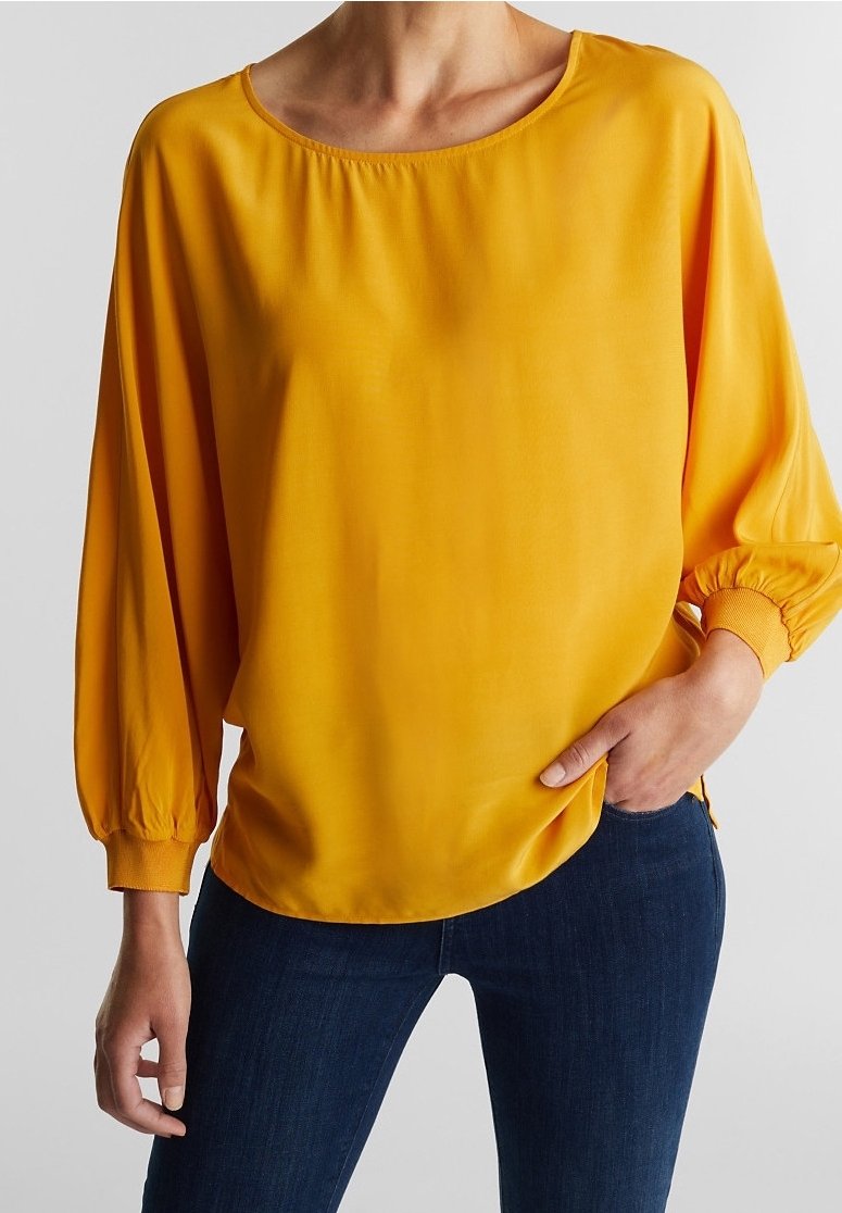 Blouse jaune légère avec un col arrondi, des manches longues ballon avec des poignets élastiques, et une coupe décontractée, associée à un jean foncé.