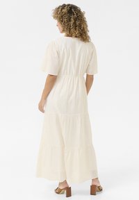 Long, tiered dress in cream fabric with a slight shimmer, gathered waist, and short puff sleeves. Paired with tan block-heeled sandals.