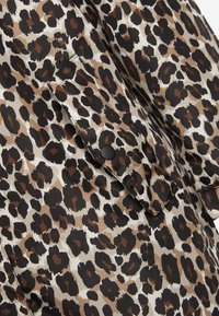 Gepardmønstret stof i nuancer af brun, sort og creme; har detaljer med sorte trykknapper; glat tekstur; let draperet design.