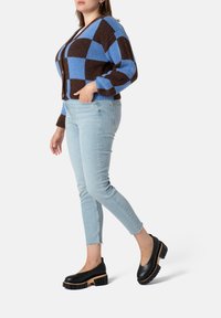 Blue and brown checkered cardigan with a relaxed fit, paired with light wash skinny jeans and black slip-on shoes with thick soles.