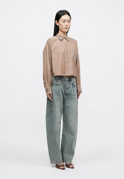 Csíkos barna és krémszínű gombos ing zsebbel; laza, kifakult kék farmerral kombinálva; a modell barna magassarkú szandált visel.