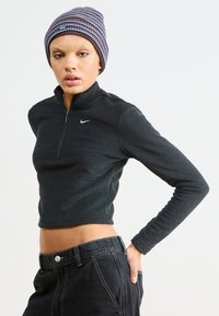 Czarna, krótsza kurtka zapinana na zamek z wysokim kołnierzem i teksturowanym materiałem, z małym białym logo Nike. W połączeniu z dżinsami o wysokim stanie.