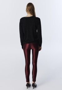 Pull noir à motif de pois blancs, associé à des leggings bordeaux brillants et des chaussures noires à petit talon, vue de dos.