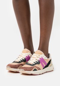 Sneaker mit einer Mischung aus hellbraunem, schwarzem und lila Wildleder sowie Leder. Das Design umfasst eine strukturierte Sohle und kontrastierende Schnürsenkel.