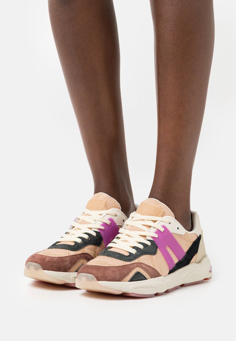 Sneaker mit einer Mischung aus hellbraunem, schwarzem und lila Wildleder sowie Leder. Das Design umfasst eine strukturierte Sohle und kontrastierende Schnürsenkel.