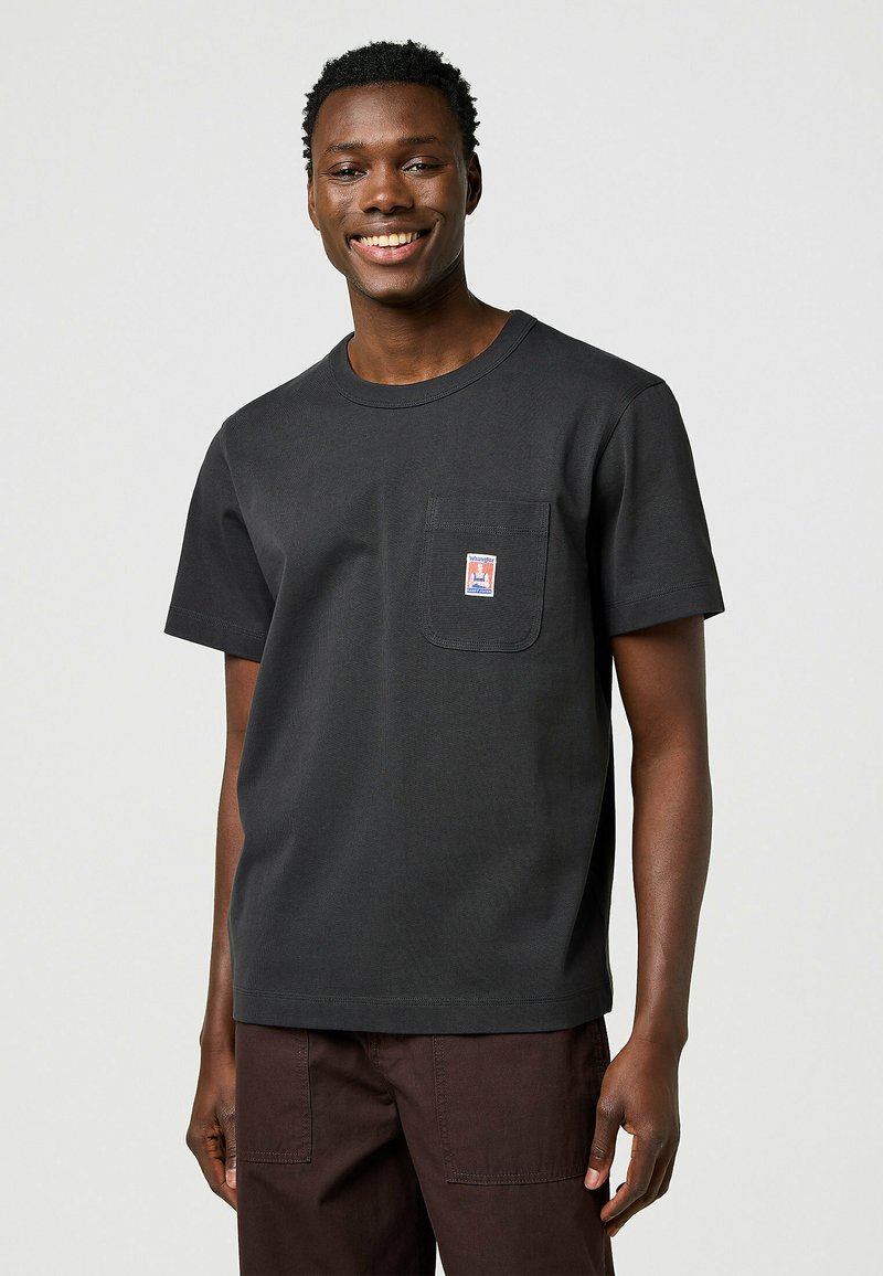 Zwarte katoenen t-shirt met een ronde halslijn, korte mouwen en een voorzak met een kleurrijk label. Eenvoudig en klassiek ontwerp.