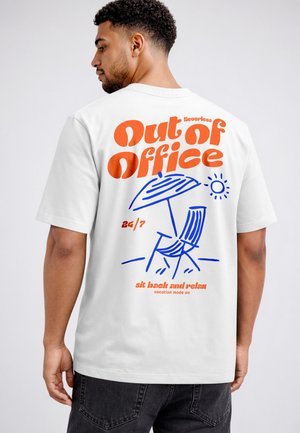 Man wearing white T-shirt with orange text "Out of Office" and blue illustration of a beach chair, umbrella, and sun on the back.