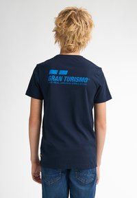 Náměsíčně modré bavlněné tričko s krátkými rukávy a kulatým výstřihem. Na zadní straně se nachází modré logo a text "Gran Turismo".