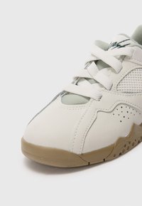 Sneaker bianco con suola beige, lacci bianchi, pannello laterale in mesh e dettagli forati vicino alla suola.