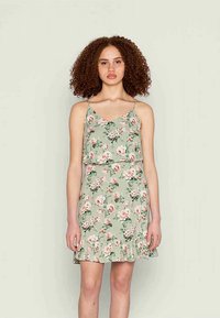 Vestido verde floral com alças de espaguete ajustáveis, bainha franzida e cintura ajustada. Apresenta um padrão de flores rosa e brancas.