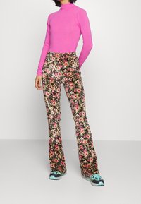 Růžový rolák s dlouhým rukávem spojený s kalhotami s vysokým pasem a rozšířenými nohavicemi, které mají květinový vzor v růžové, červené a zelené na tmavém pozadí.