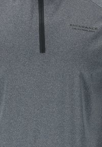 Grå halvdraget pullover med texturerad tyg, som har en svart dragkedja och logodetalj i övre vänstra hörnet. Avslappnad atletisk design.