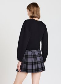 Maglione nero lavorato a maglia con maniche a palloncino abbinato a una gonna plissettata grigia a quadri con dettagli neri e viola.