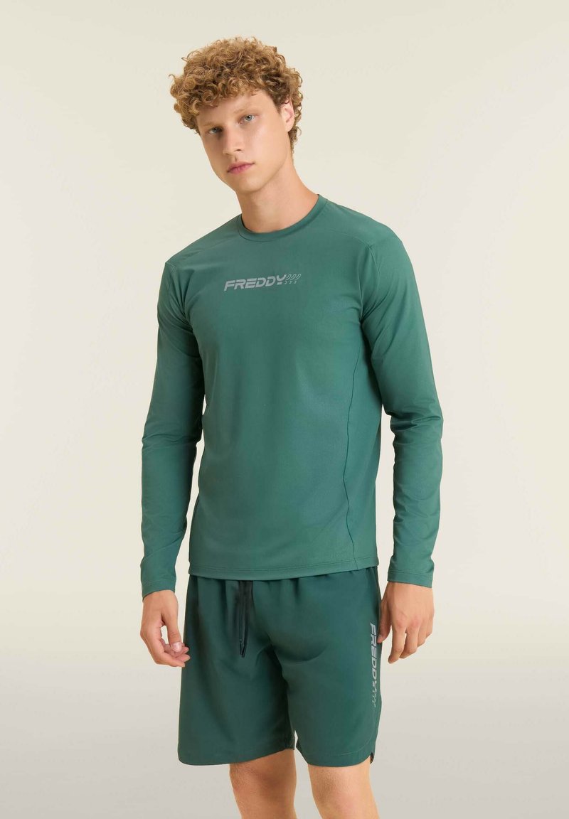 Chemise verte à manches longues en tissu lisse avec un design ajusté. Présente un logo sur la poitrine ; assortie avec un short accordé.