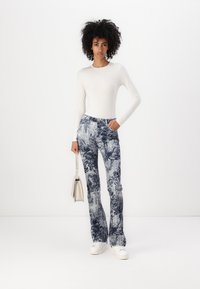 Hvit langermet topp kombinert med blå mønstrede flagrende jeans med detaljerte design. Kombinert med hvite sneakers og en liten sølvveske.