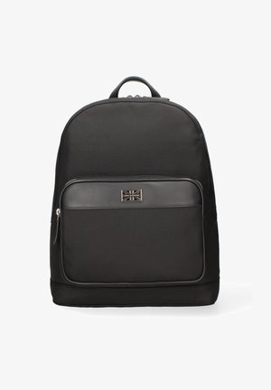 Sac à dos noir avec un extérieur en tissu texturé, une poche zippée à l'avant et une plaque de logo en métal arborant un motif de Union Jack. Forme arrondie.