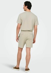 Camiseta de punto beige de manga corta y pantalones cortos a juego con dos bolsillos traseros, llevados con zapatos marrones con cordones, vistos desde la espalda.