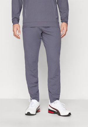Graue Sporthosen mit Slim Fit, leichtem Stoff und elastischem Bund, kombiniert mit weißen Turnschuhen mit roten Akzenten.