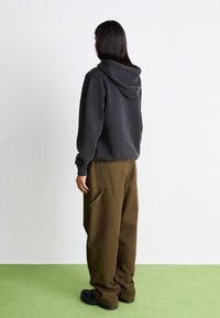 Mørkegrå hættetrøje med en stor hætte, parret med rummelige olivengrønne bukser med sidelommer. Sorte sko fuldender outfittet.