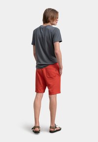 T-shirt grigio a maniche corte e pantaloni corti di cotone rossi. I pantaloni hanno una tasca posteriore con una cucitura decorativa. Sandali con cinturini regolabili.