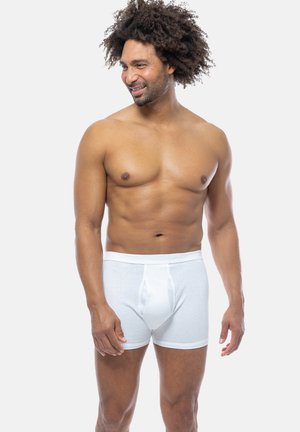 Witte katoenen boxershorts met een ribbelstructuur, voorzien van een voorvak en een elastische tailleband, gemodelleerd door een shirtloze man.