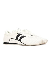 Zapatillas blancas con rayas negras, parte superior de cuero texturizado, diseño de cordones, suela curvada y detalle de logo sutil en el lateral.