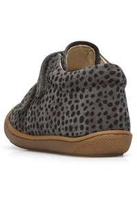 Zapato de ante gris con puntos negros, con forma redondeada y un collar suave. Suela de goma texturizada para agarre y flexibilidad. Cierre de velcro.