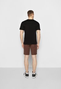 Černé tričko s krátkým rukávem a hnědé šortky s hladkým povrchem. Bílé a černé tenisky. Neutrální pozadí.