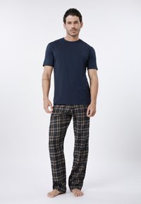 Tamsiai mėlynas medvilninis marškinėlis derinamas su ruda ir tamsiai mėlyna languota pižamos kelnėmis, turinčiomis elastingą juosmenį ir laisvą prigludimą. Basomis stovintis.