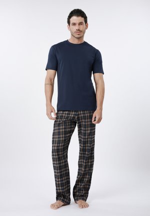 Tmavomodré bavlnené tričko v kombinácii s hnedo-modrými károvanými pyžamovými nohavicami s elastickým pásom a voľným strihom. Stojí bosý.